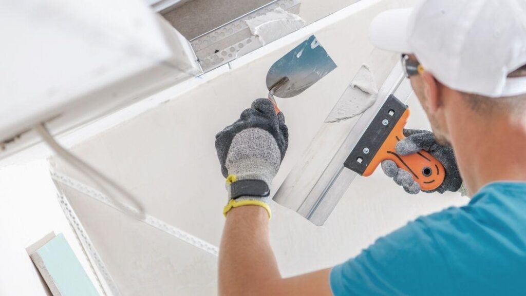 A worker using a trowel to patch drywall, applying plaster to a hole in the wall for a smooth finish.