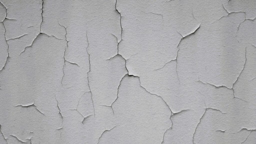 Cracked plaster walls with peeling paint and widespread surface cracks forming irregular patterns across a worn interior wall.