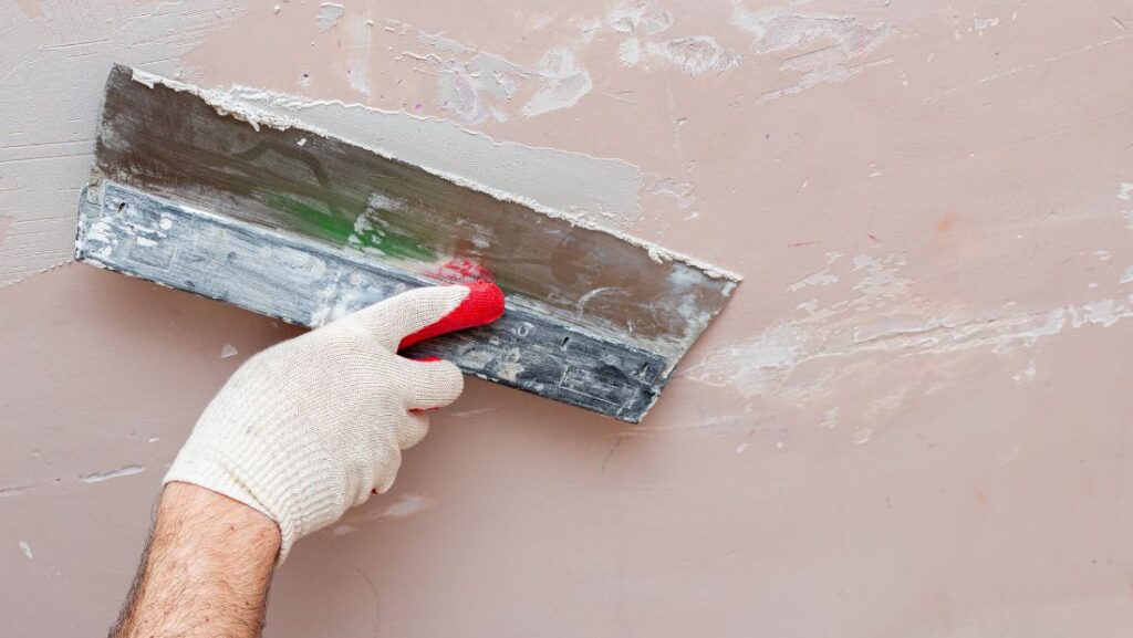 A person performing wall repairs, smoothing out plaster with a trowel to fix wall imperfections.