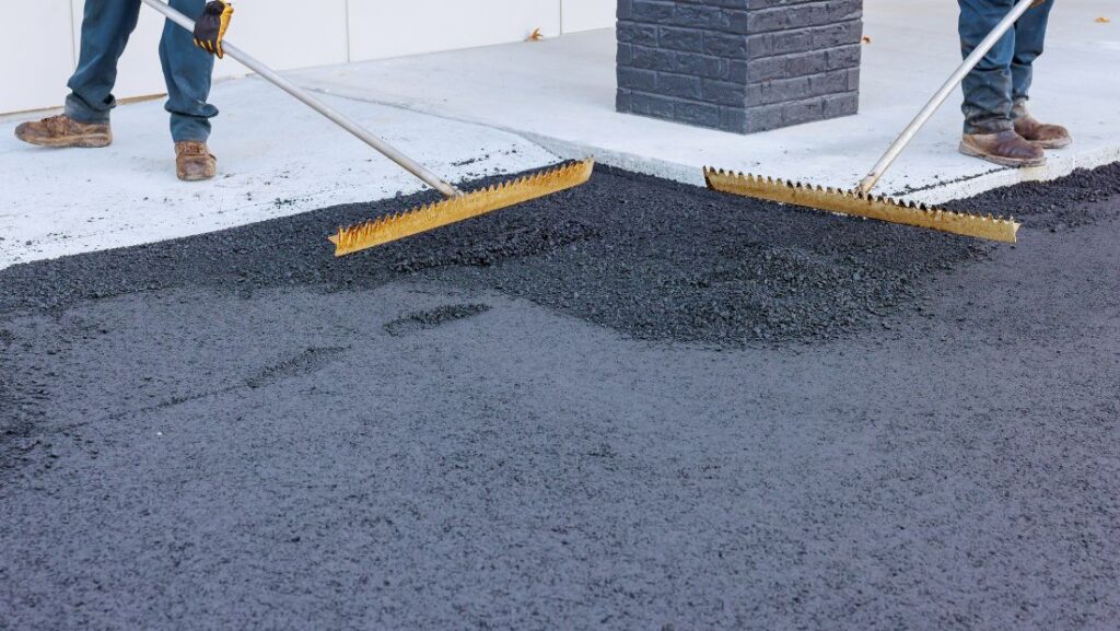 Workers using rakes to spread and level fresh asphalt mix during parking lot repair
