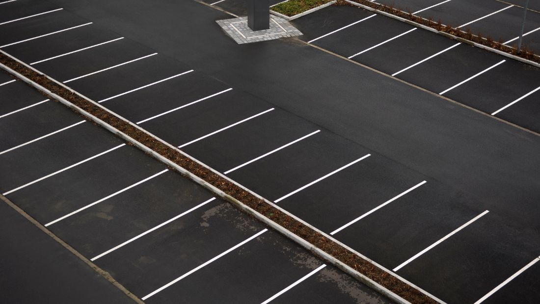 Aerial view of a freshly paved asphalt parking lot with clean white painted parking space lines and empty stalls.
