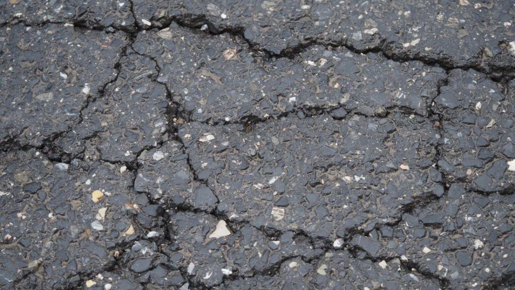 Close-up view of severely cracked asphalt surface showing alligator cracking, illustrating pavement deterioration and damage relevant to how to repair an asphalt parking lot and structural asphalt failure.